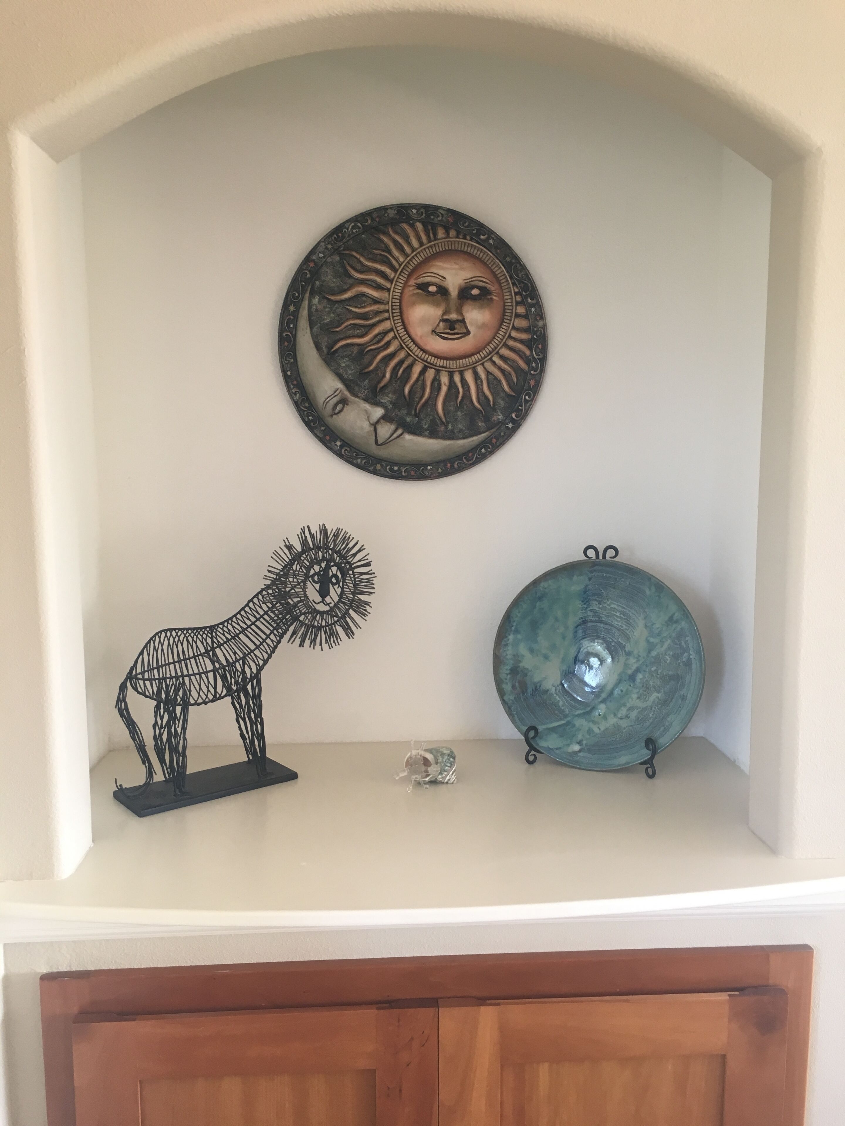 Una pared con un detalle decorativo de metal con un sol y una luna, una escultura de metal de un león y un plato de cerámica.