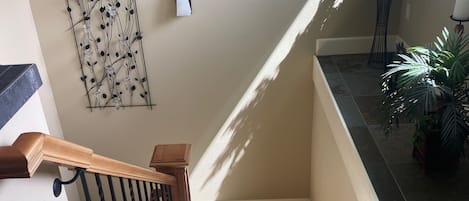 A carpeted staircase with a wooden handrail and black balusters, leading to a landing with a wall-mounted light fixture and a decorative wall art piece.
