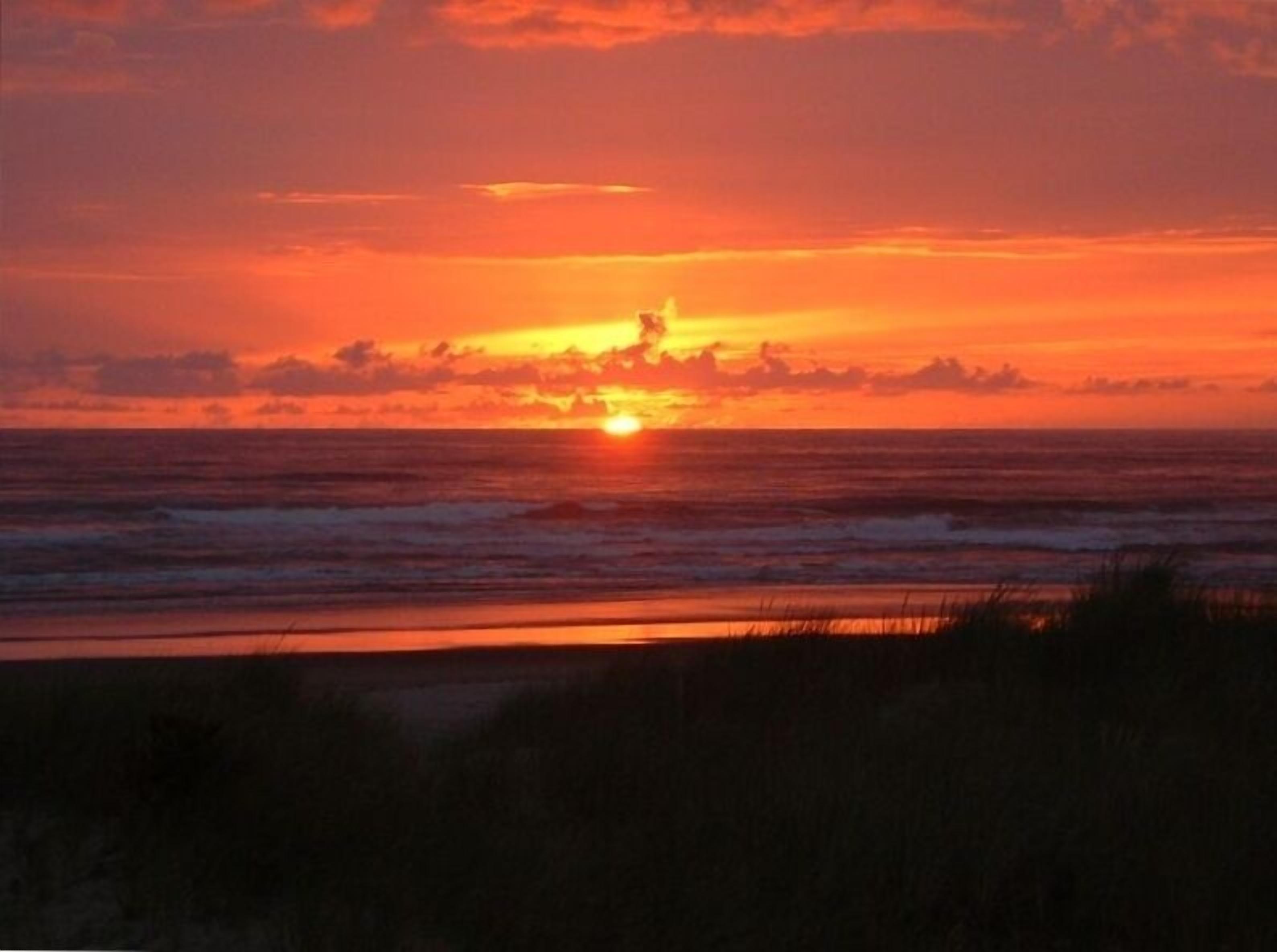 A sunset over the ocean with a beach in the foreground.