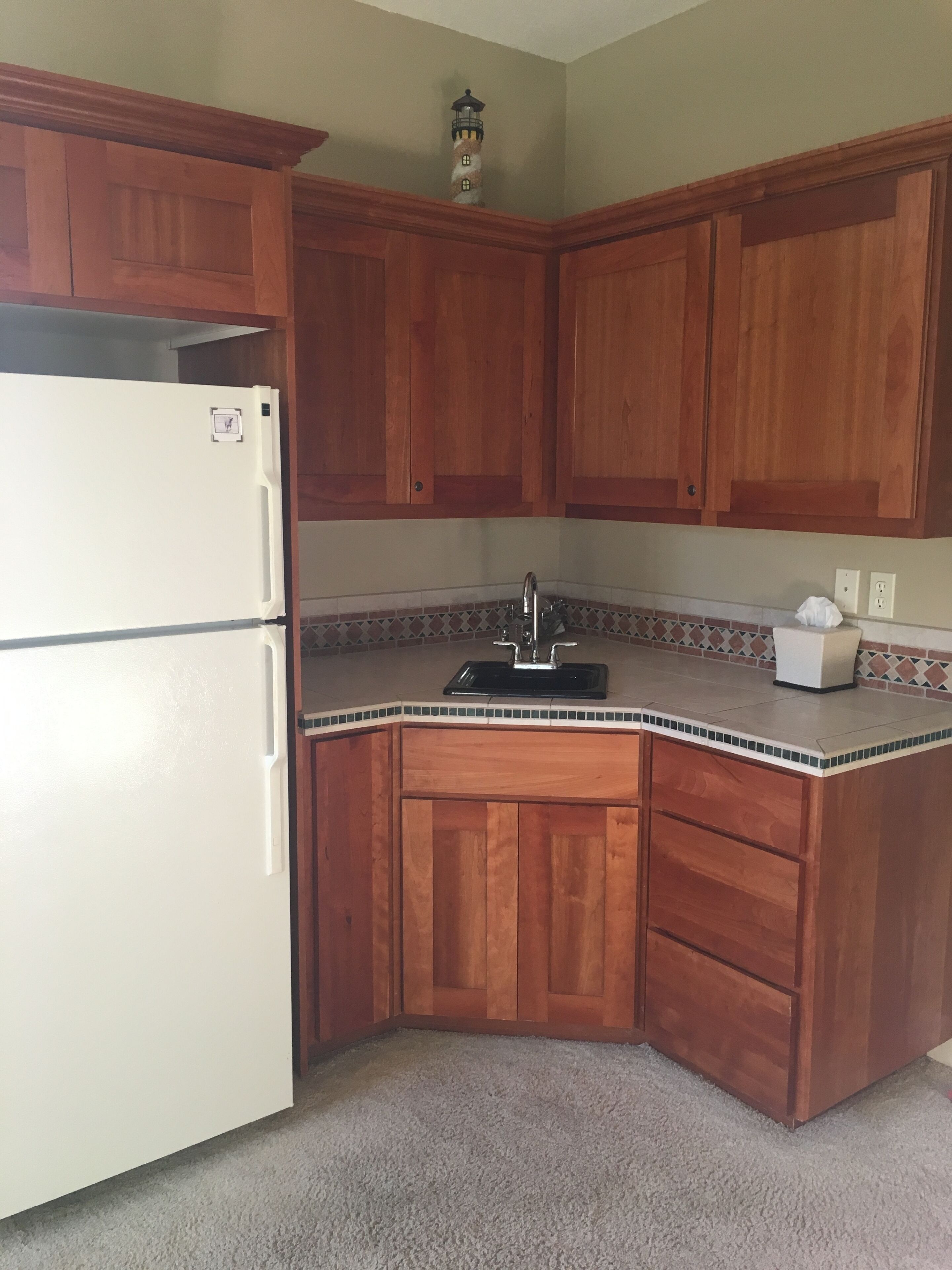 Una cocina con armarios de madera, un refrigerador blanco, un lavamanos y un faro decorativo.