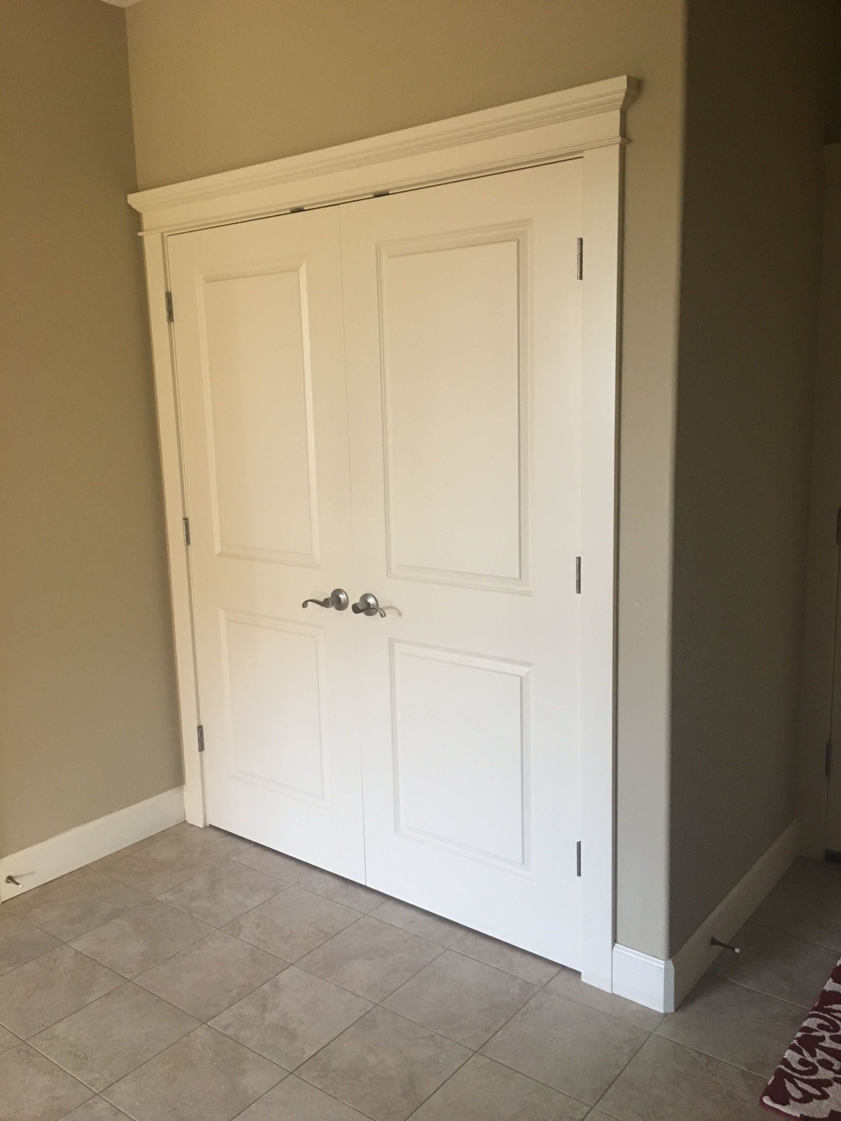 A closed white door with a silver handle, a tiled floor, and a plain wall.