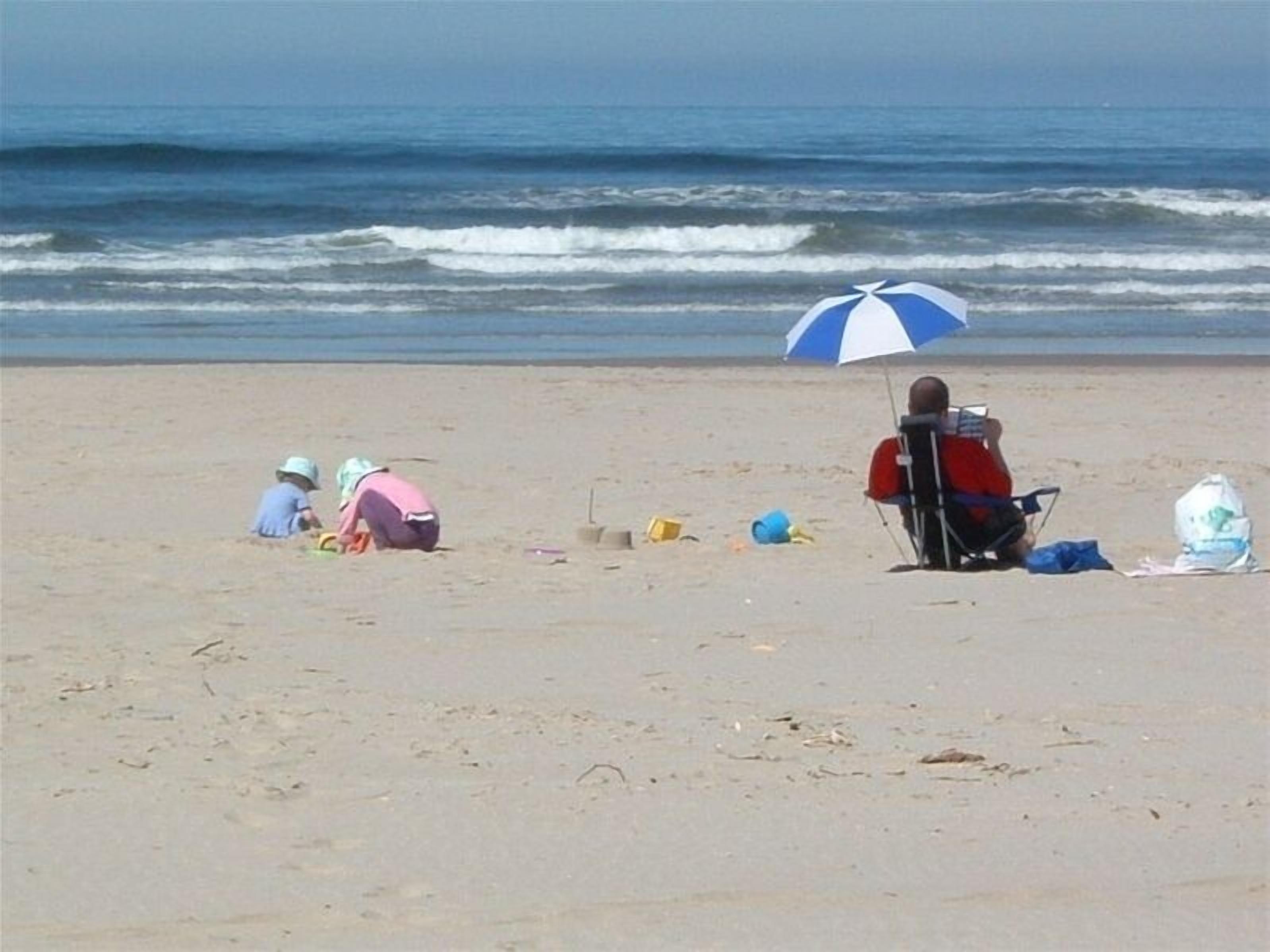 A beach scene with people sitting and playing.
