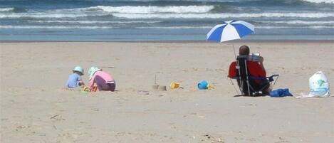 A beach scene with people sitting and playing.