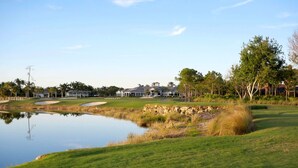 A golf course with a pond, sand bunkers, and a clubhouse in the background.