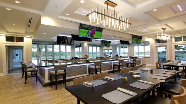 A modern restaurant with multiple dining tables and chairs, a bar area with a counter, and large windows providing a view of the outdoors.