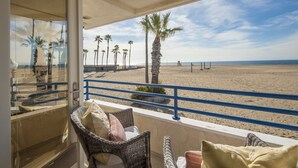 Ein Balkon mit Korbmöbeln, Blick auf einen Strand mit Palmen und einem klaren Himmel.