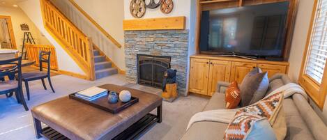 A living room with a stone fireplace, a large flat-screen TV, a sofa, and a wooden staircase.
