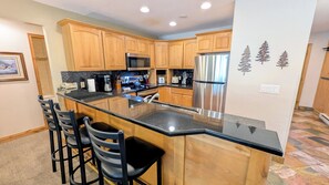 A kitchen with wooden cabinets, a stainless steel refrigerator, a microwave, and a granite countertop.