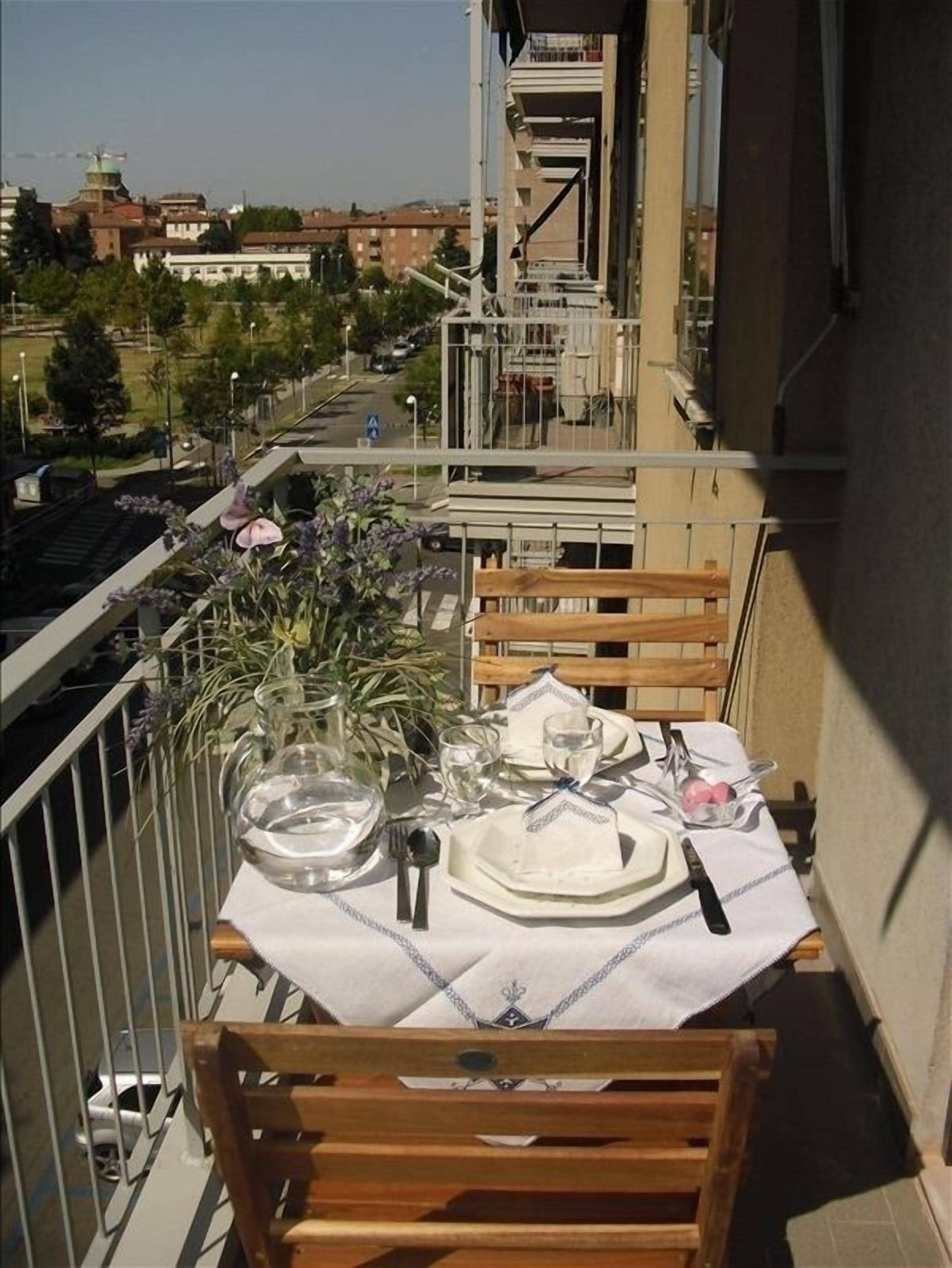 A balcony with a table set for two, overlooking a cityscape.