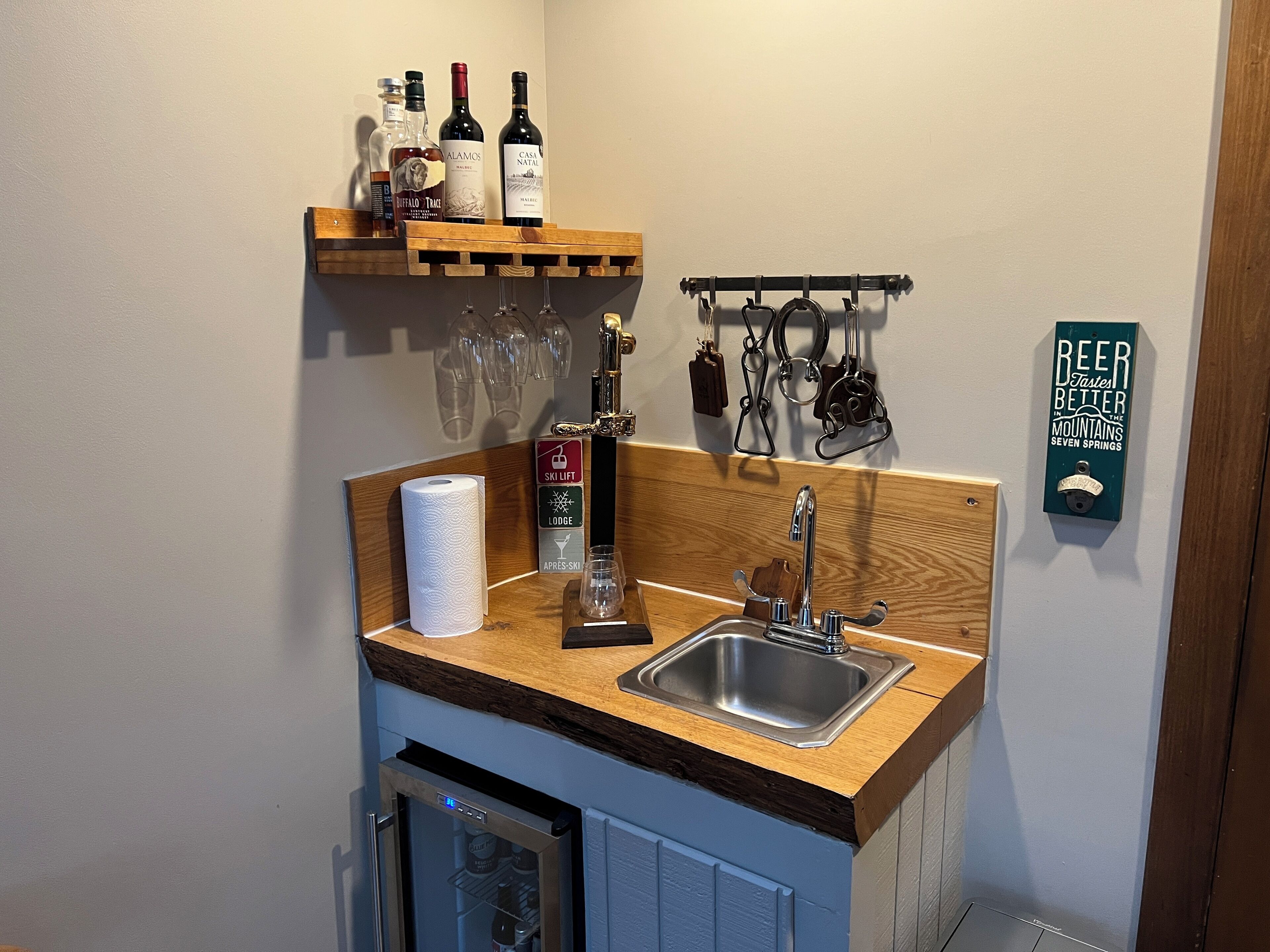 A compact kitchen with a wooden countertop, a stainless steel sink, and a wine bottle holder.