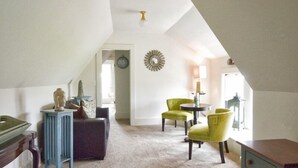 A spacious attic room with a high ceiling, a clock, a decorative wall piece, and a cozy seating area with a table and chairs.