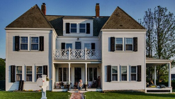 A two-story house with a front porch, a covered entryway, and a small garden area.
