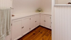 A room with wooden flooring, white cabinetry, a skylight, and a small shelf.