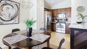 A modern kitchen with stainless steel appliances, a dining area with a round table and placemats, and a large abstract painting on the wall. - The "Pool Cottage" Upgraded Home FREE Heated Pool (Phoenix)