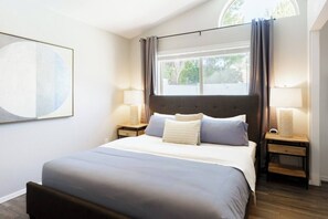 Une chambre à coucher bien rangée, avec un grand lit, deux tables de chevet et une fenêtre avec des rideaux.
