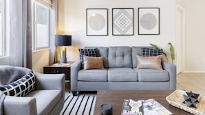 A modern living room with a grey sofa, a black and white armchair, a striped rug, and a coffee table with magazines and a basket. - The "Pool Cottage" Upgraded Home FREE Heated Pool (Phoenix)