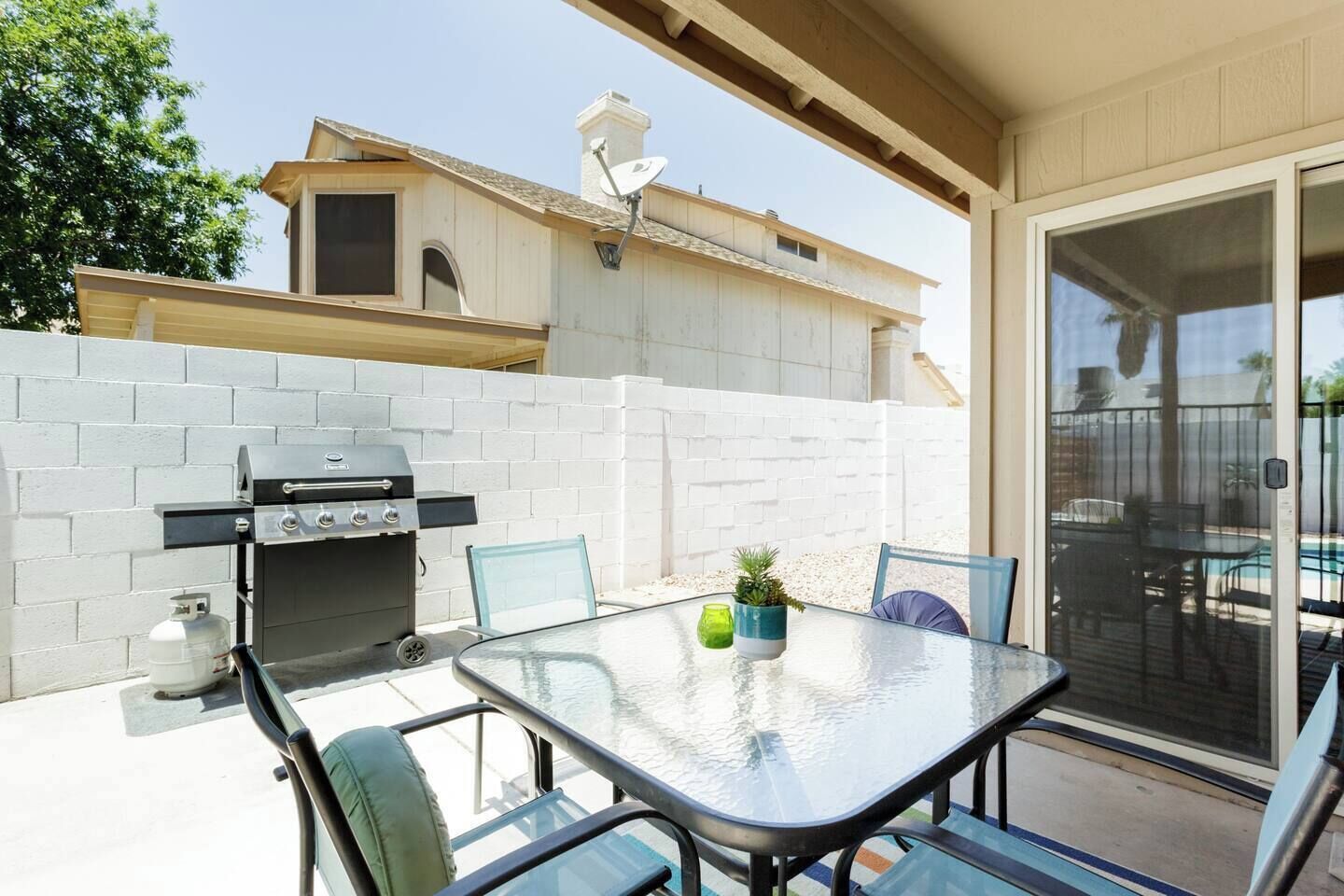 An outdoor patio with a grill, a table with chairs, and a view of a house in the background.