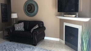 A living room with a black leather sofa, a round mirror, a flat-screen TV, a fireplace, and a decorative wall piece. - Great location!! Pool! Unit 5201- Mtn. View Condos, 3 Bed, 2 Bath (Pigeon Forge)