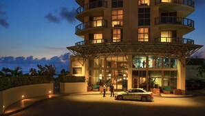 A multi-story hotel with a glass facade, a covered entrance, and a car parked in front.