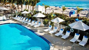 A poolside area with lounge chairs and umbrellas, a beach in the background, and a clear view of the ocean.