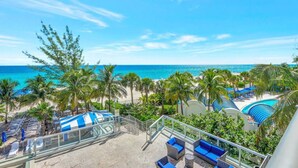A beachside resort with a pool area, lounge chairs, and palm trees.