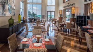 A spacious dining area with high ceilings and large windows, featuring a modern interior design with wicker chairs and a polished wooden floor.