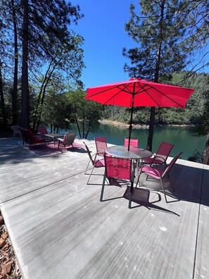 A deck with outdoor furniture, a red umbrella, and a view of a lake surrounded by trees. - This home has it all and more!! Message me for video tour! (Lakehead)
