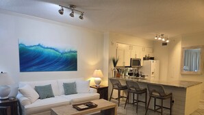 Ein Wohnzimmer mit einer Couch, einem Couchtisch und einer Küchenzeile mit einer Bar und Stühlen.
