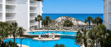 A resort with a pool, palm trees, and a view of the ocean.