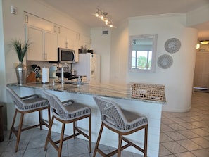 A kitchen with a central island, bar stools, a microwave, and a refrigerator.