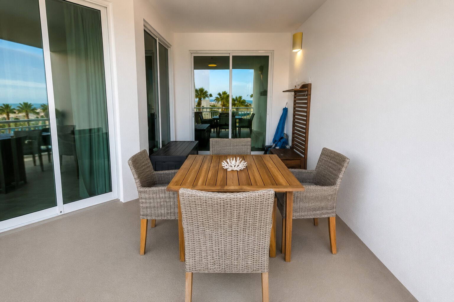Un balcón con mesa y sillas, una puerta corrediza de vidrio y vistas a palmeras.