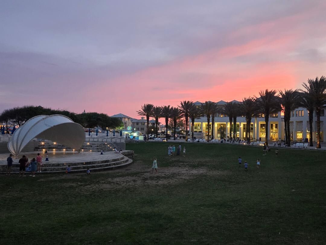 Un'ampia area esterna con una struttura moderna e imponente, palme e edifici sullo sfondo.