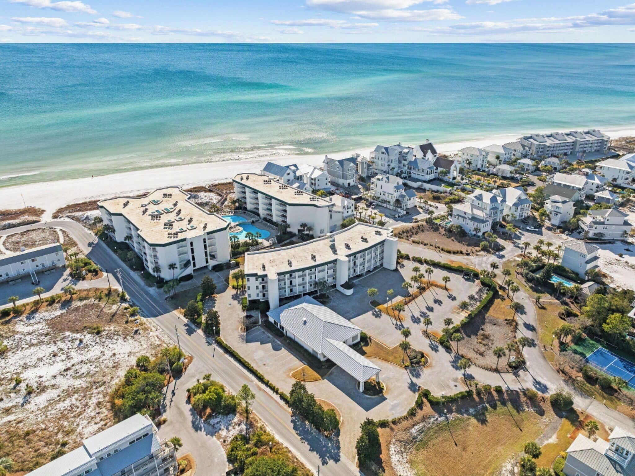 An aerial view of a coastal resort with multiple buildings, a beach, and a clear blue sea.