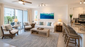 Ein modernes Wohnzimmer mit Sofa, Sesseln, Couchtisch und einer Küchenzeile mit Bar und Arbeitsplatte.