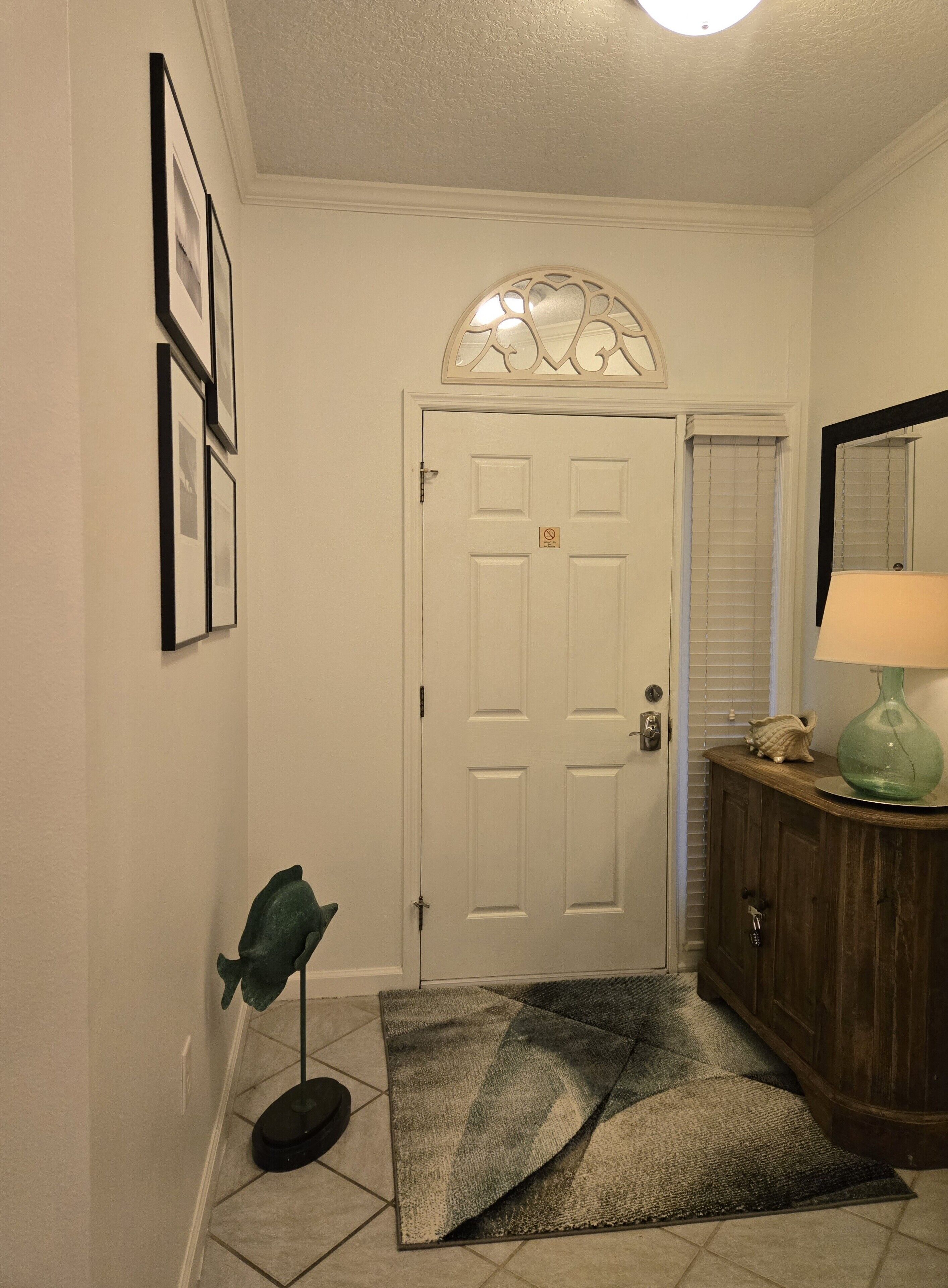 Un couloir avec une porte blanche, un petit tapis, un lampadaire vert et un meuble en bois sur lequel est posée une lampe.