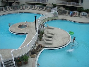 A large, multi-curve swimming pool with a hot tub and lounge area, surrounded by lounge chairs and umbrellas.