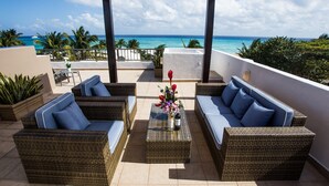 A covered outdoor seating area with wicker furniture and a view of the ocean.