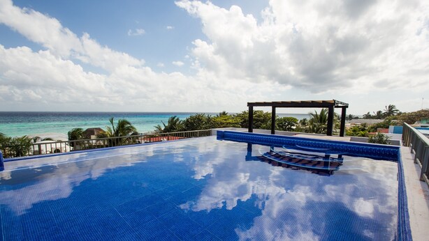 A clear blue infinity pool with a wooden pergola and a view of the ocean.