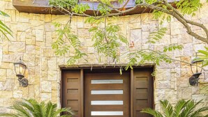 A stone building with a large wooden door, two potted plants, and a tiled entrance. - Welcome to Casa Caiman | FULL STAFFED + 2 BOATS by Viridian Experience (peninsula papagayo)