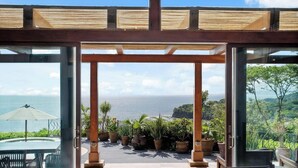 A glass-enclosed patio with a view of the ocean, wooden pergola, and potted plants. - Welcome to Casa Caiman | FULL STAFFED + 2 BOATS by Viridian Experience (peninsula papagayo)
