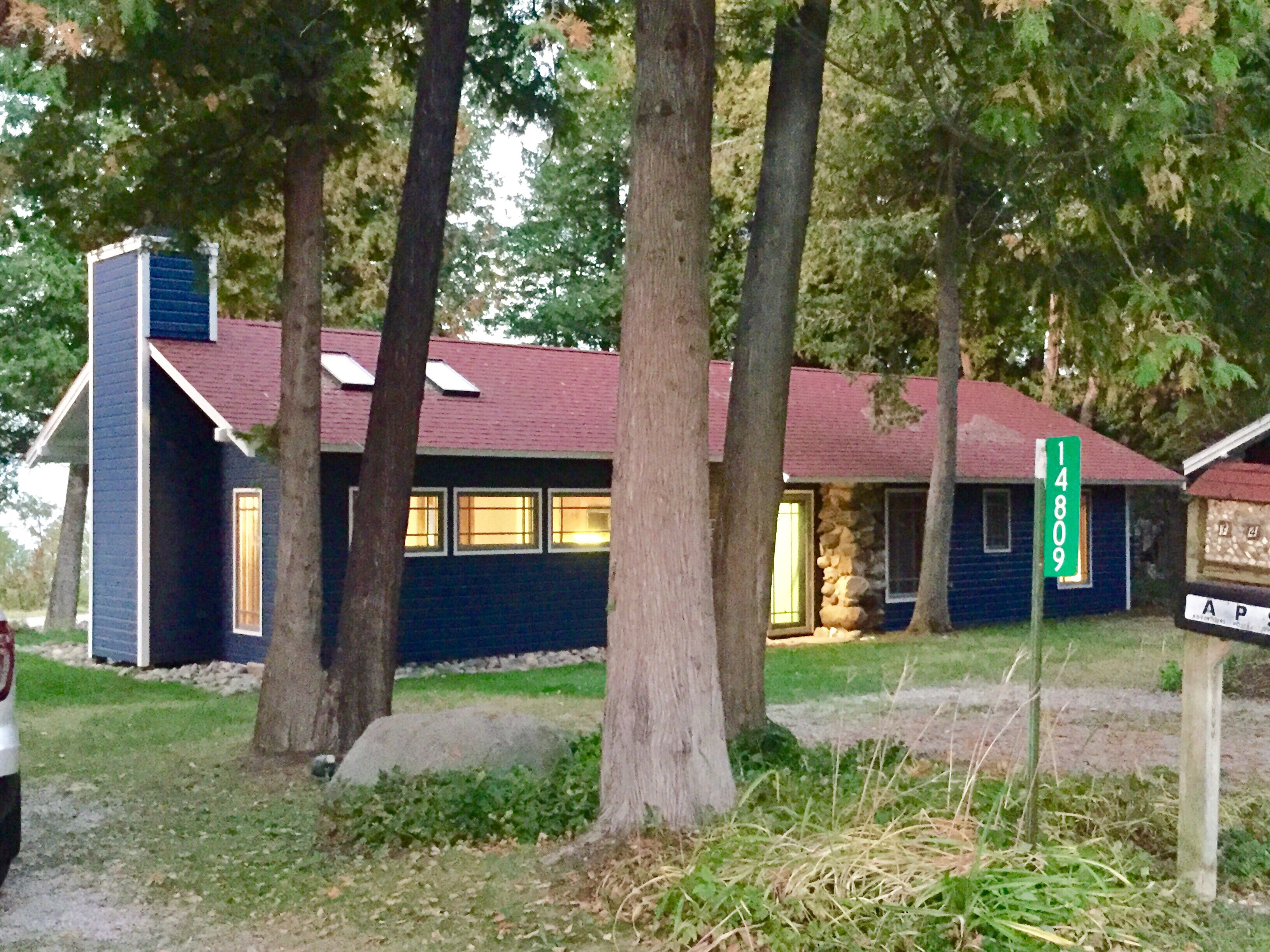 A small, single-story building with a dark blue exterior, a red roof, and a chimney. There is a green street sign with the number 14809.
