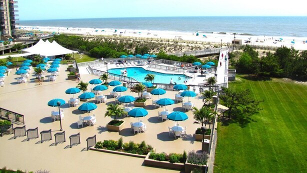 Ein Resort mit Poolbereich, Blick auf den Strand und Sitzgelegenheiten im Freien mit Sonnenschirmen.