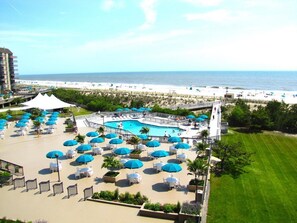A resort with a pool area, beach view, and outdoor seating with umbrellas.
