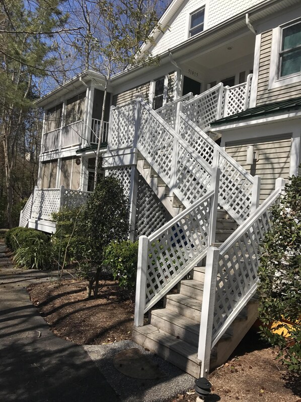 A two-story house with a white exterior, a front porch, and a wooden staircase with a lattice railing.