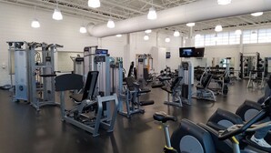 Ein Fitnessstudio mit verschiedenen Trainingsgeräten, einem großen Spiegel und einem Fernseher an der Wand.
