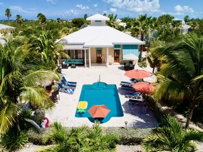 A pool area with lounge chairs and umbrellas, surrounded by palm trees and a building with a white roof. - You Know you want to be Here!/Sleeps 6/Private Pool and Fun Tiki Bar! (Providenciales)