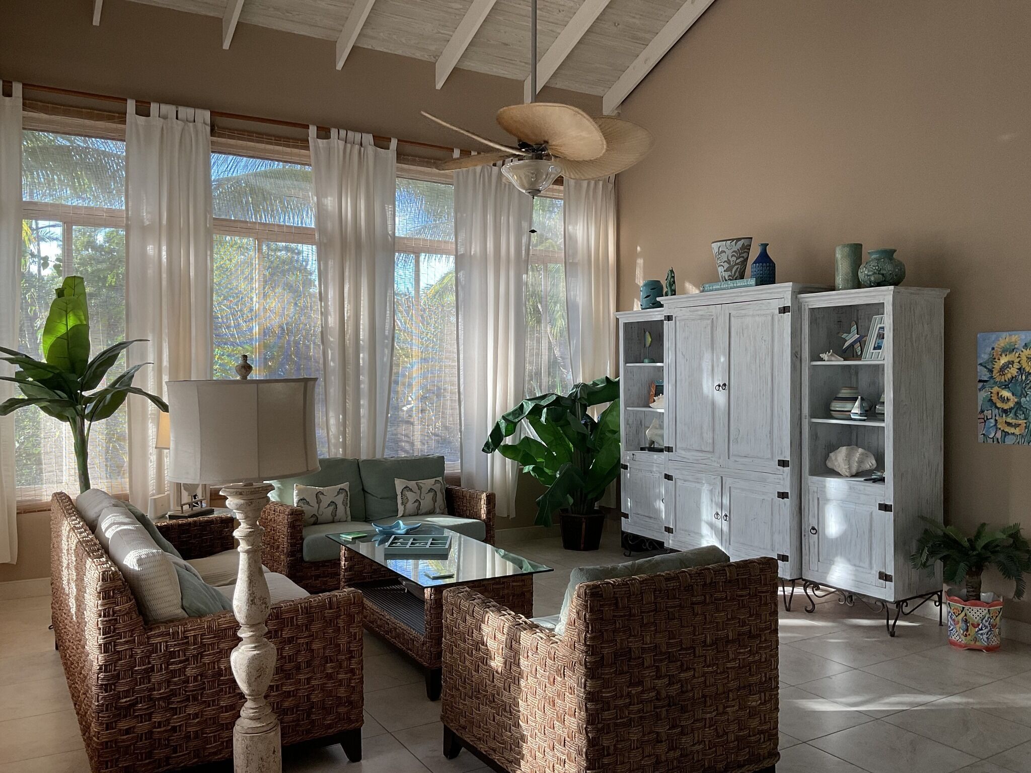 Una sala de estar con muebles de mimbre, una mesa de centro de vidrio y un mueble aparador con estantes.