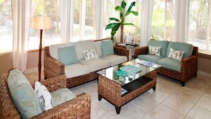 Ein geräumiges Wohnzimmer mit Korbmöbeln, großen Fenstern und einem Deckenventilator.