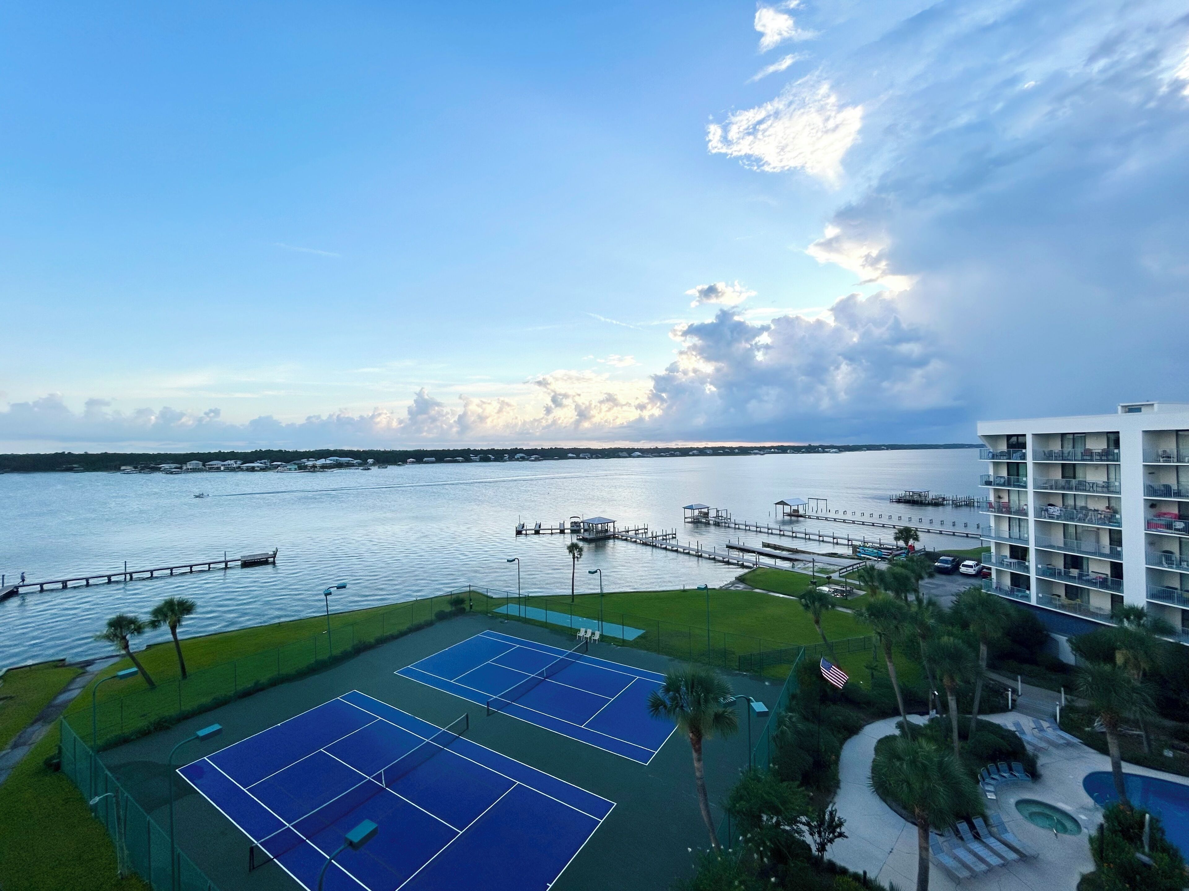 Una cancha de tenis con vista al agua y un edificio con balcones.