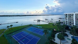 Un court de tennis avec vue sur l’eau et un bâtiment doté de balcons.